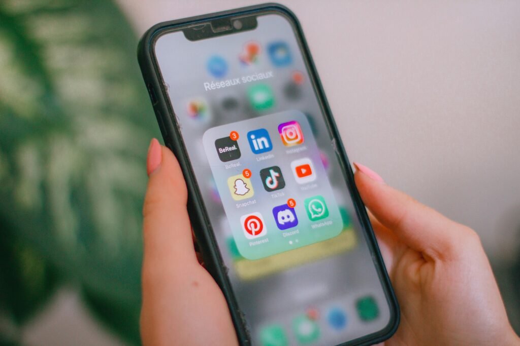 Hands holding a phone showing a folder of social media apps – social media management